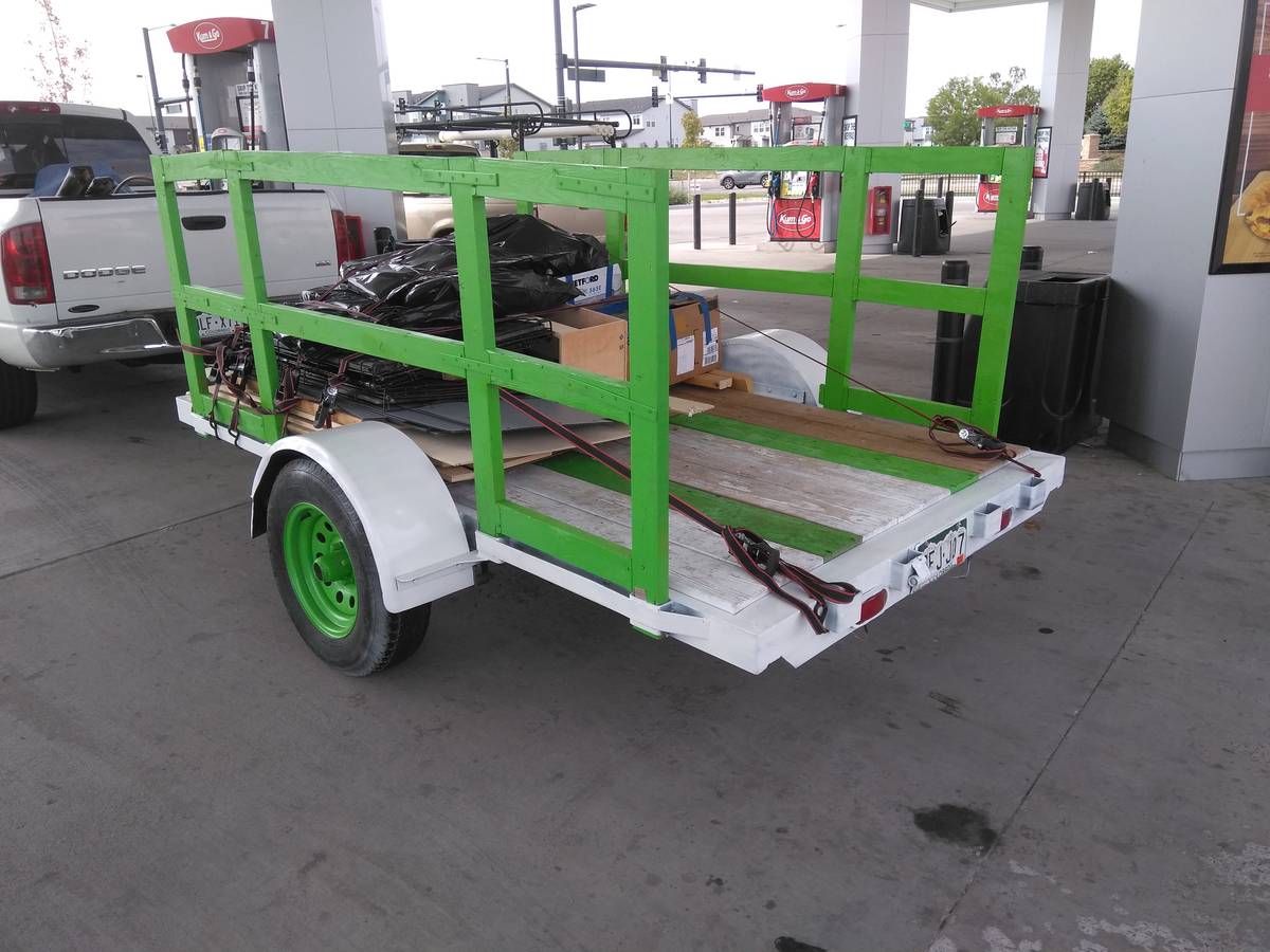 Open utility trailer with green rails loaded with debris at gas station